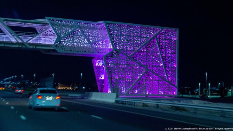 Angular Dubai building illuminated in purple and magenta at night.