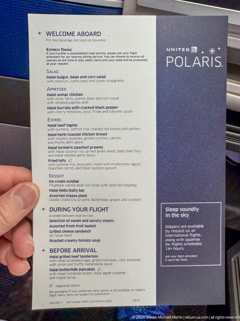 Hand pointing at a printed airline safety card beside an aircraft seat.