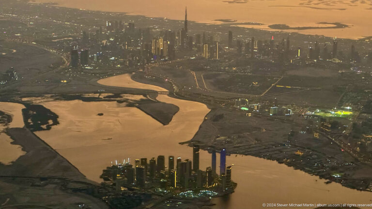 Aerial sunset view of winding waterways and Dubai’s distant skyline.