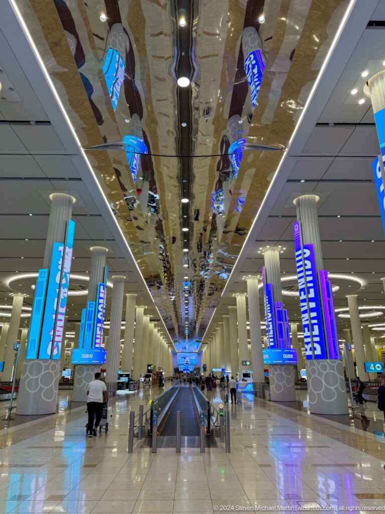 Wide Dubai airport concourse with blue digital displays and polished floors.