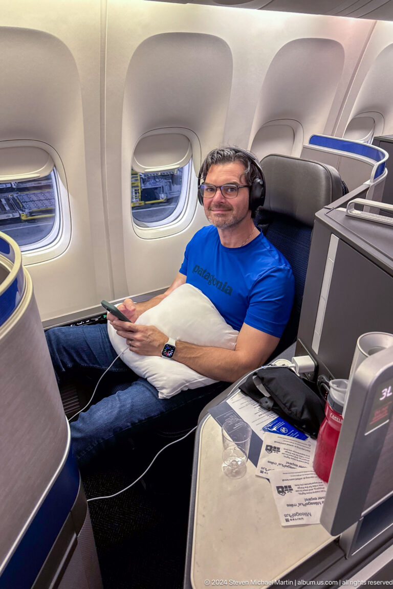 Man in a blue shirt seated in a spacious airplane seat.