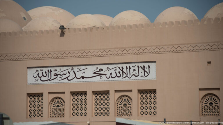 Mosque façade with Arabic inscription above decorative windows.