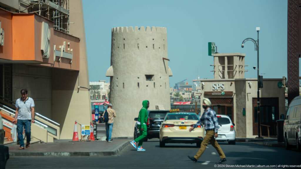 Busy street scene beside a round historic watchtower in Dubai.