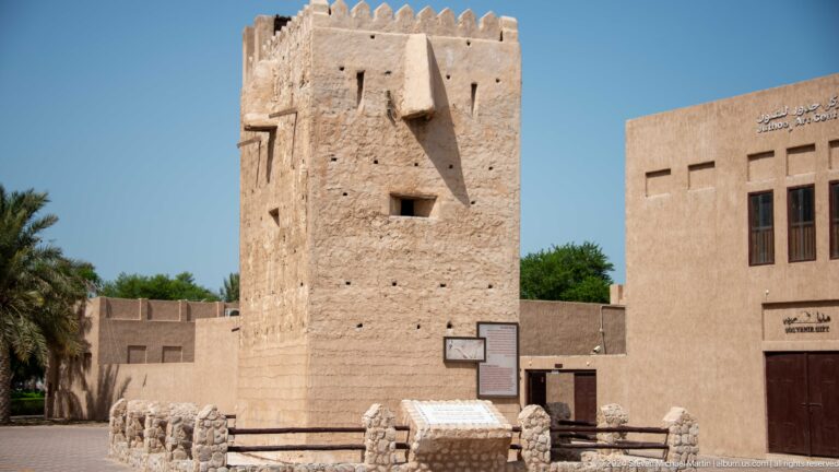 Square sand-colored watchtower among heritage buildings in Dubai.