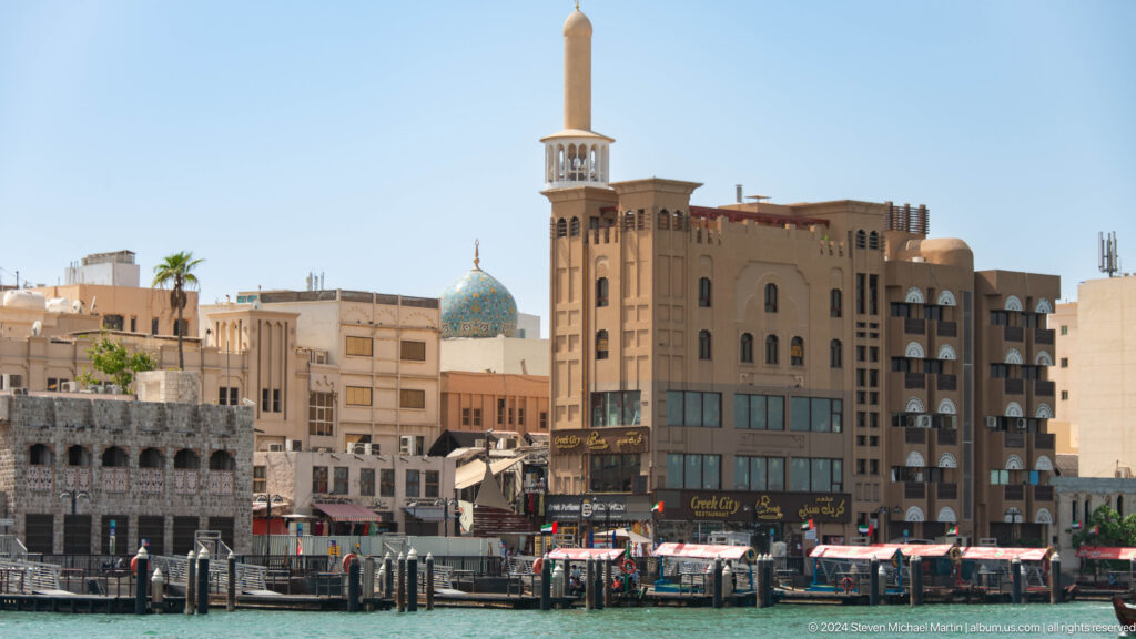Creekside buildings and boats beneath a tall square mosque minaret.