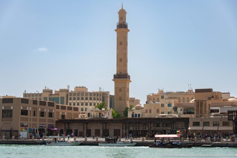 Dubai Creek waterfront with a tall mosque minaret above low buildings.