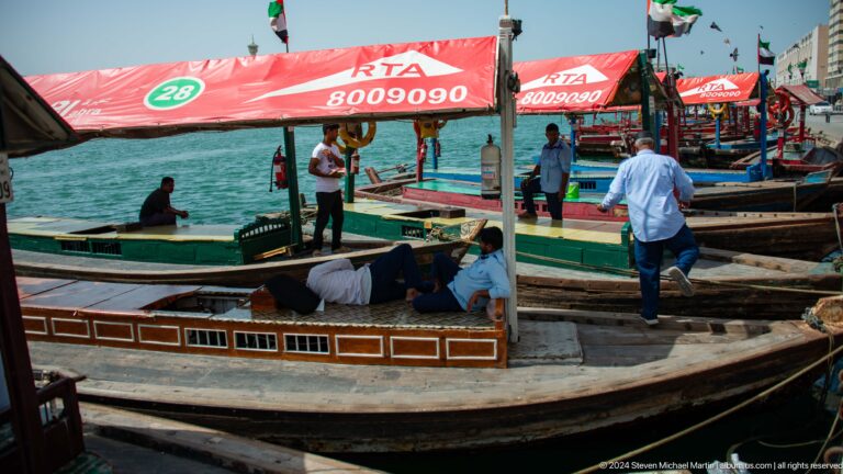 Abra landing with wooden boats, red canopies, and people on Dubai Creek.