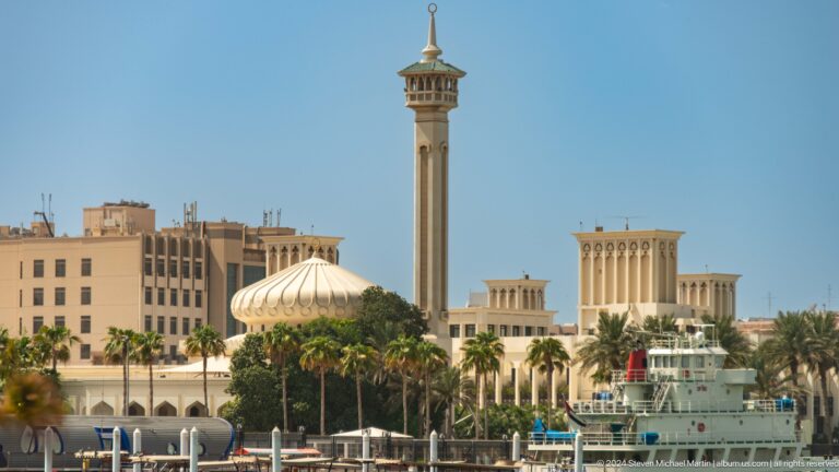 Mosque dome, minaret, wind towers, and boat along Dubai Creek.