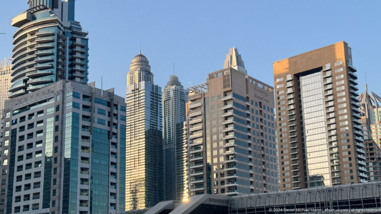 Dense cluster of Dubai residential towers with blue glass and beige façades.