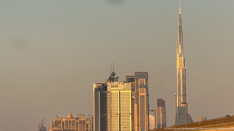Burj Khalifa rising behind shorter Dubai towers in warm haze.