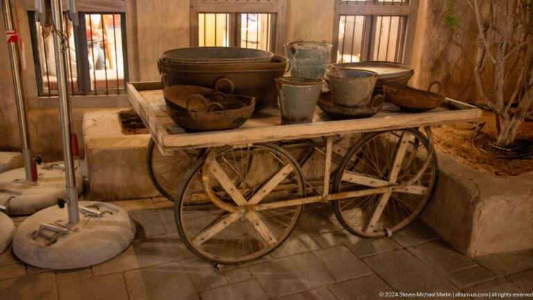 Old wooden cart with large spoked wheels carrying several clay pots and jars in a heritage display setting at Al Seef.