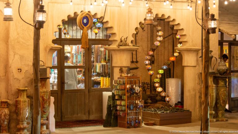 Warmly lit heritage-style craft shop interior at Al Seef in Dubai with shelves of decorative merchandise surrounding a central geometric mirror set into a textured wall.