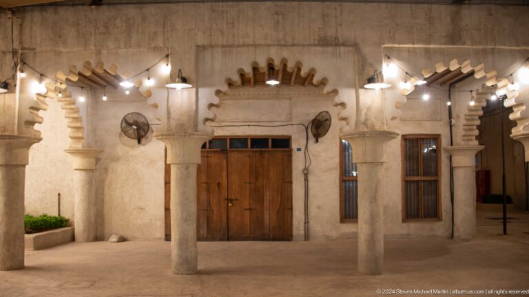 Frontal view of a heavy wooden double door framed by thick plaster columns and a scalloped decorative arch in Al Seef, Dubai.