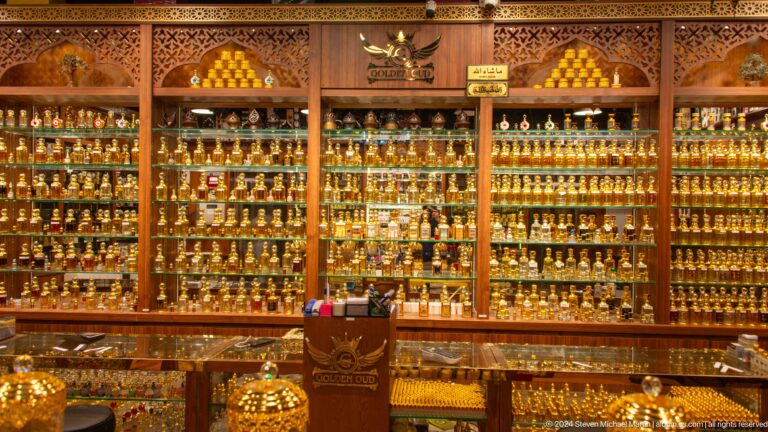 Rows of small ornate glass perfume bottles packed tightly on shelves under warm golden light in a market shop at Al Seef, Dubai.