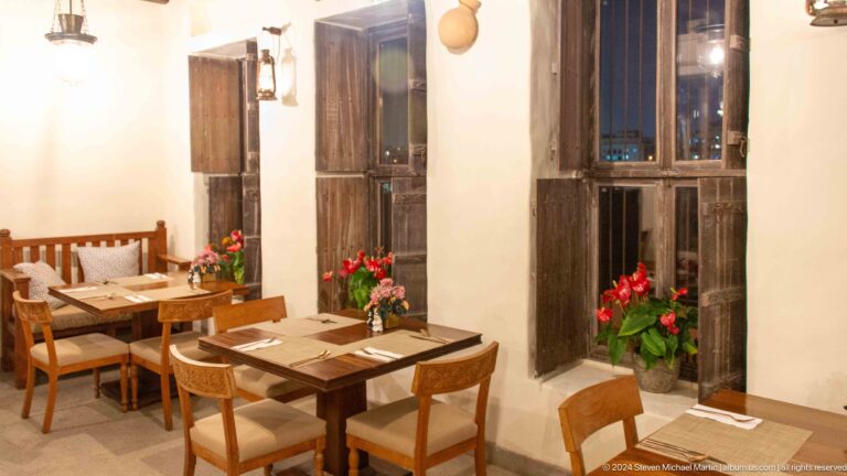 Heritage restaurant dining area at Al Seef in Dubai with a set wooden dining table, chairs, and tall dark timber shutters along the wall.