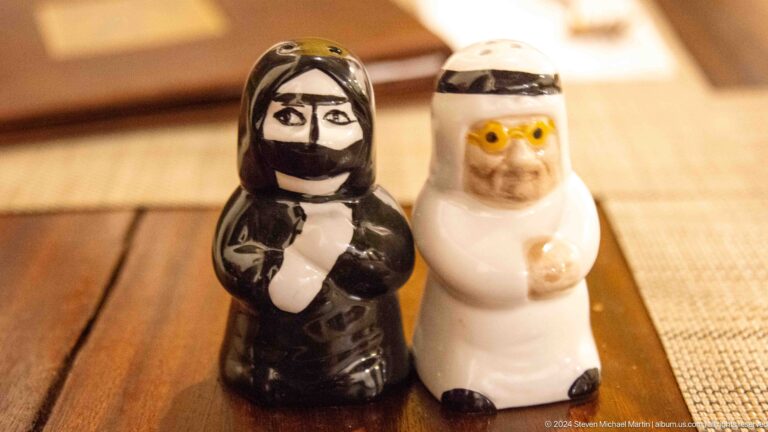 Two small souvenir figurines in stylized traditional Emirati clothing, one in black and one in white, standing side by side on a surface.