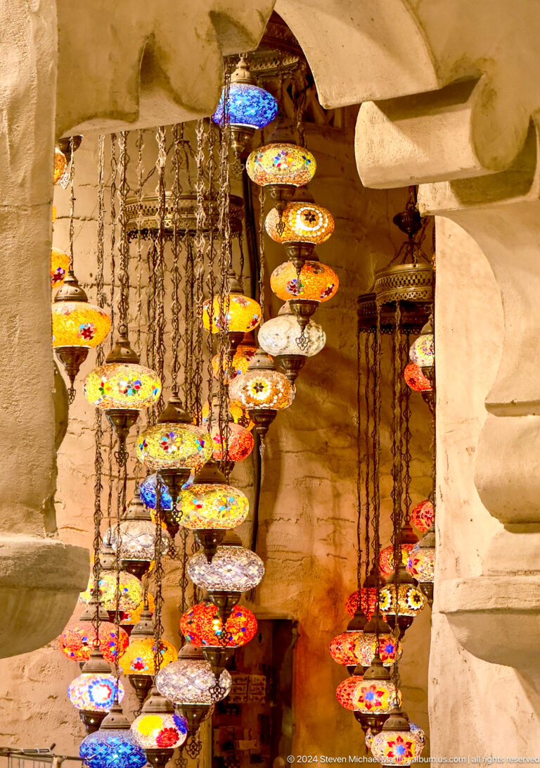 Multiple hanging mosaic glass lamps with multicolored geometric panels glowing against a rough wall in an Al Seef shop in Dubai.