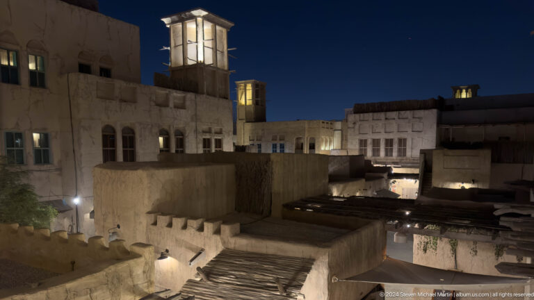 Elevated night view of Al Seef’s low plaster rooftops and scattered warm lights forming a compact heritage district under a dark sky.