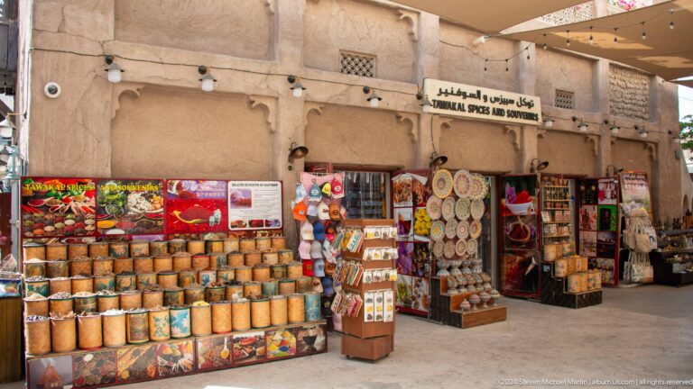 Traditional open-front market shop in Al Seef, Dubai, with large woven baskets and brightly colored goods displayed beneath bilingual Arabic-English signage.