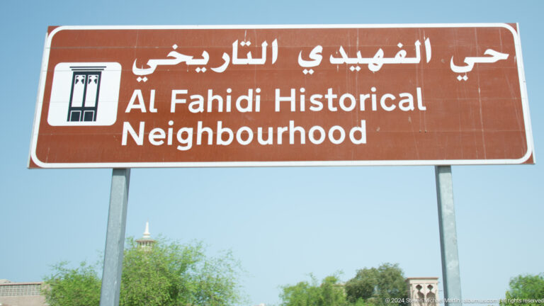 Brown bilingual directional sign reading “Al Fahidi Historical Neighbourhood” with Arabic script and an arrow.