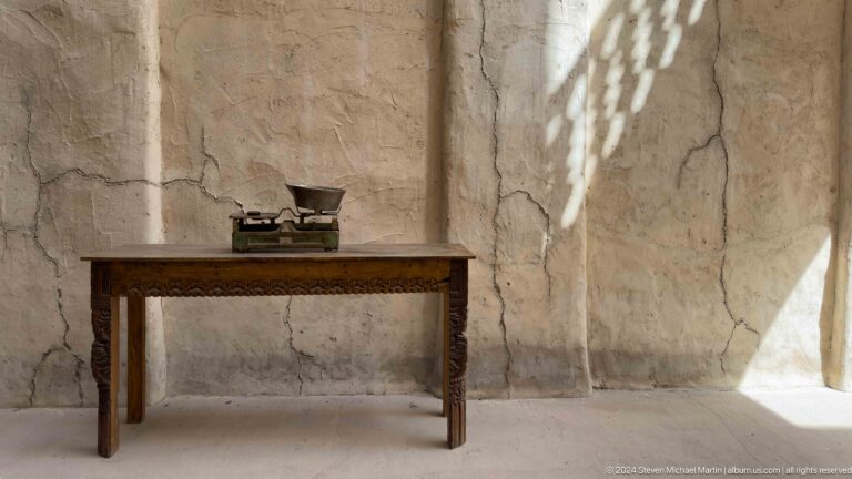 Small vessel on a narrow wooden table against a cracked plaster wall in an Al Fahidi heritage interior in Dubai.
