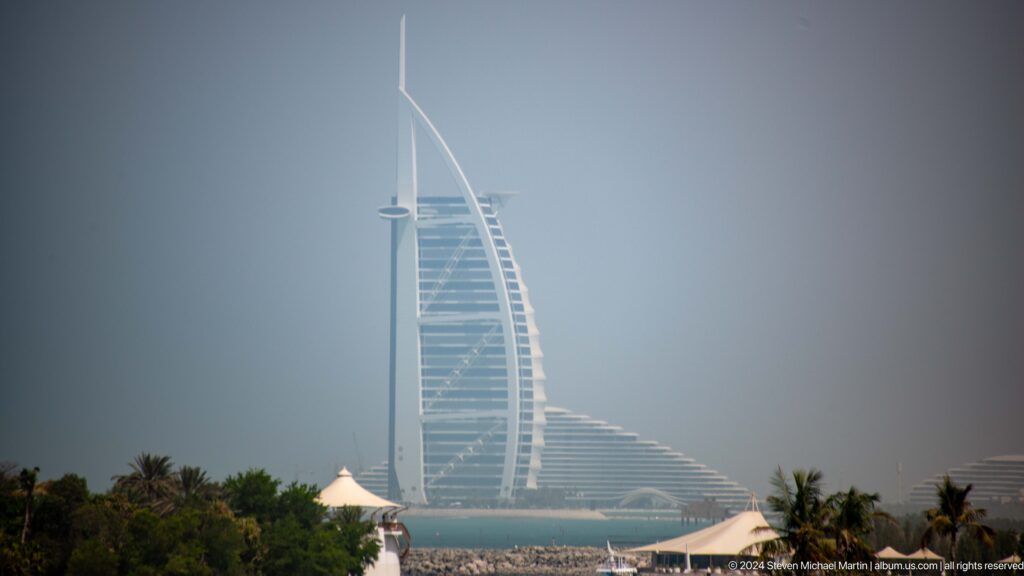 Burj Al Arab hotel seen beyond palms and white resort canopies from Palm Jumeirah.