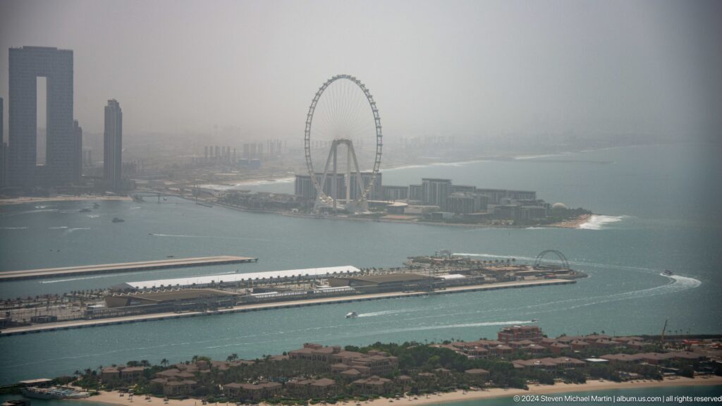 Ain Dubai observation wheel and Bluewaters Island seen across hazy coastal water.