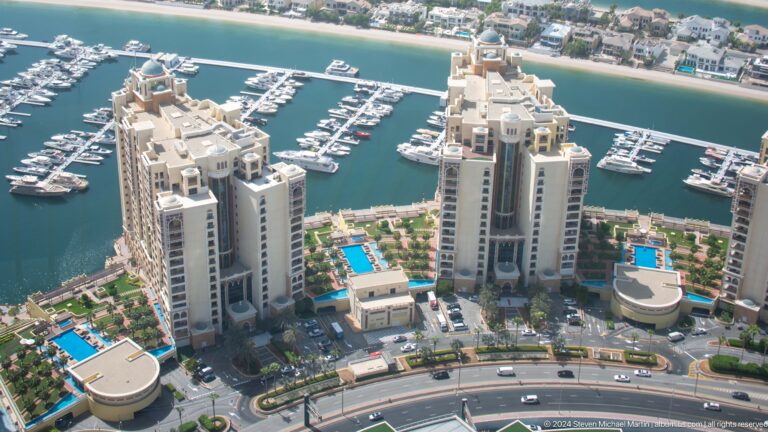 High-angle view of twin beige towers, blue pools, and a yacht marina on Palm Jumeirah.