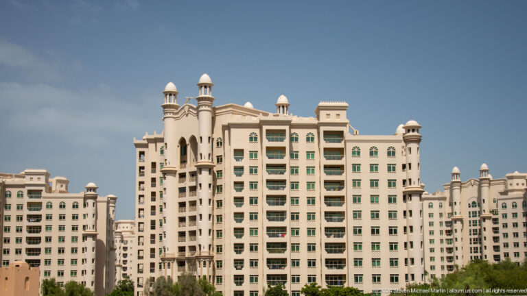 Beige Palm Jumeirah apartment tower with rows of balconies and small domed turrets.