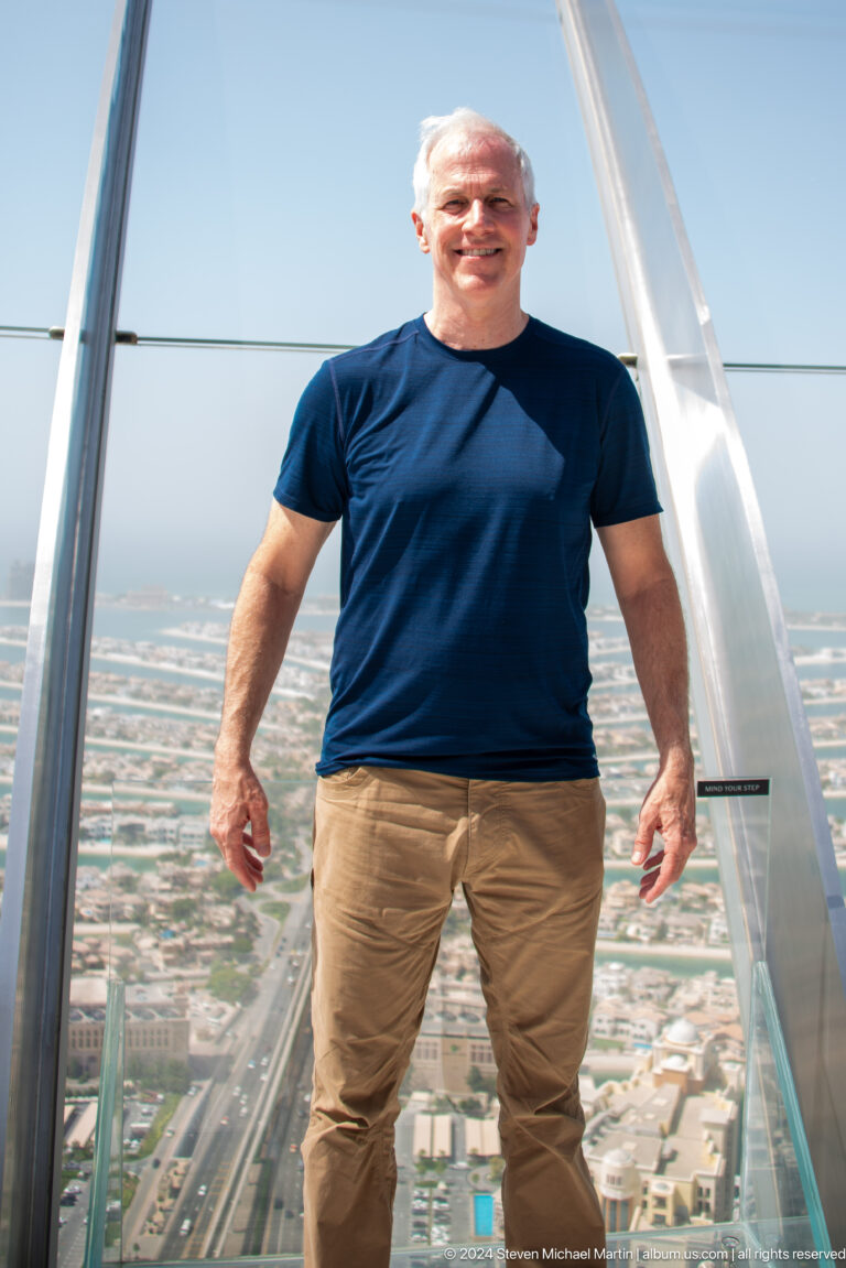Torso of a man in a navy shirt at a high observation deck over Palm Jumeirah.