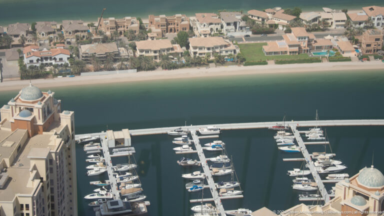 Yacht marina below a sandy beach and row of Palm Jumeirah villas.