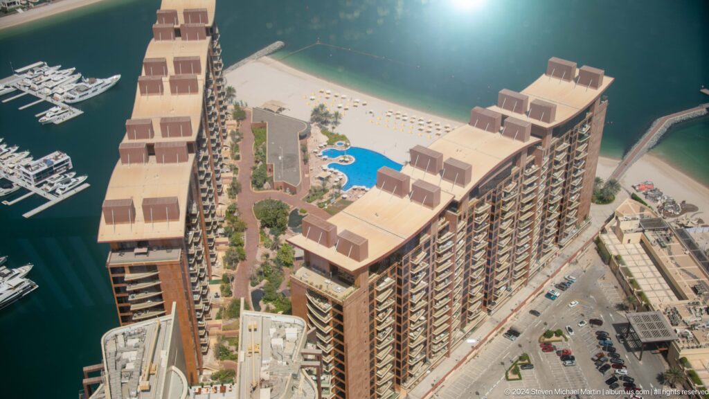 Long Palm Jumeirah apartment block beside a blue pool, sandy beach, and calm water.
