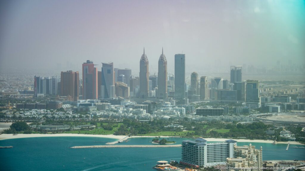 Hazy Dubai Marina skyline of clustered skyscrapers seen across coastal water.