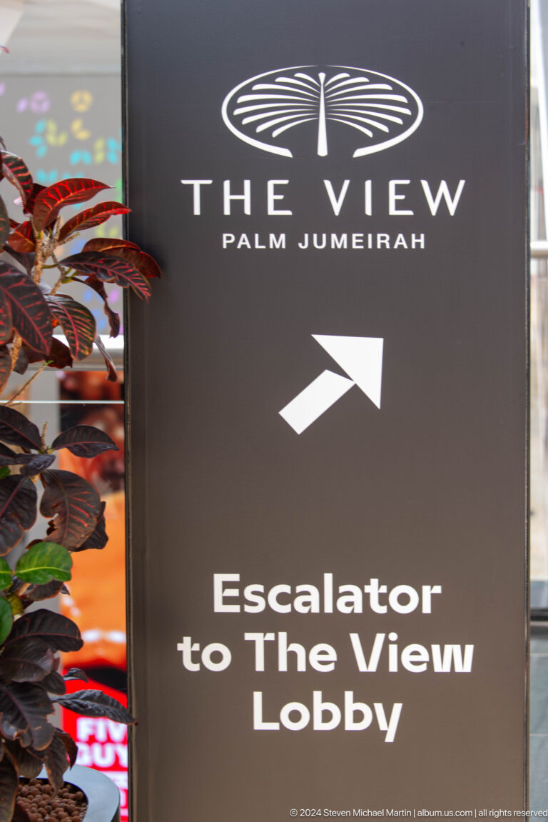 Black Palm Jumeirah sign with a white arrow pointing toward an escalator.