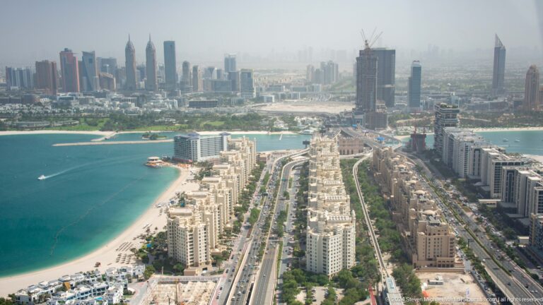 Palm Jumeirah trunk boulevard lined with apartment towers, beach, and construction.