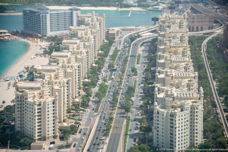 Busy Palm Jumeirah boulevard lined with ornate cream apartment towers.