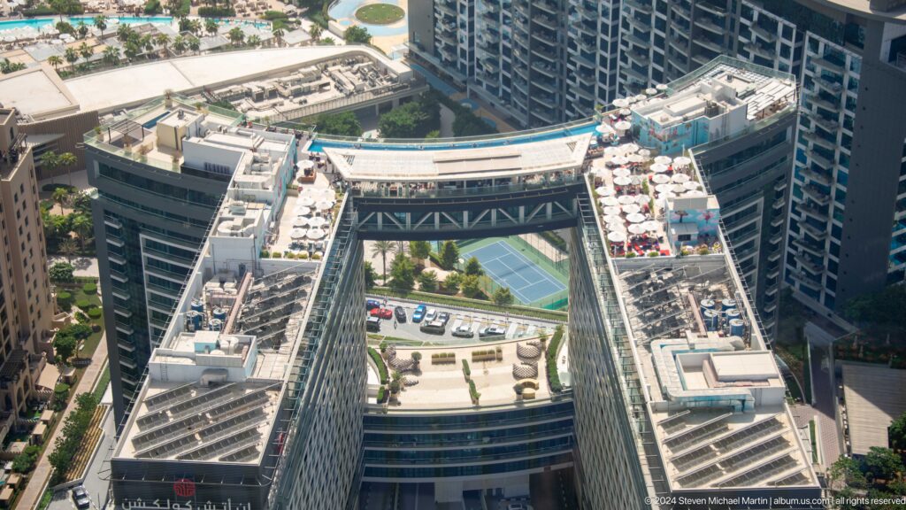 High-angle view of a Palm Jumeirah complex with a skybridge, rooftop terraces, and tennis court.