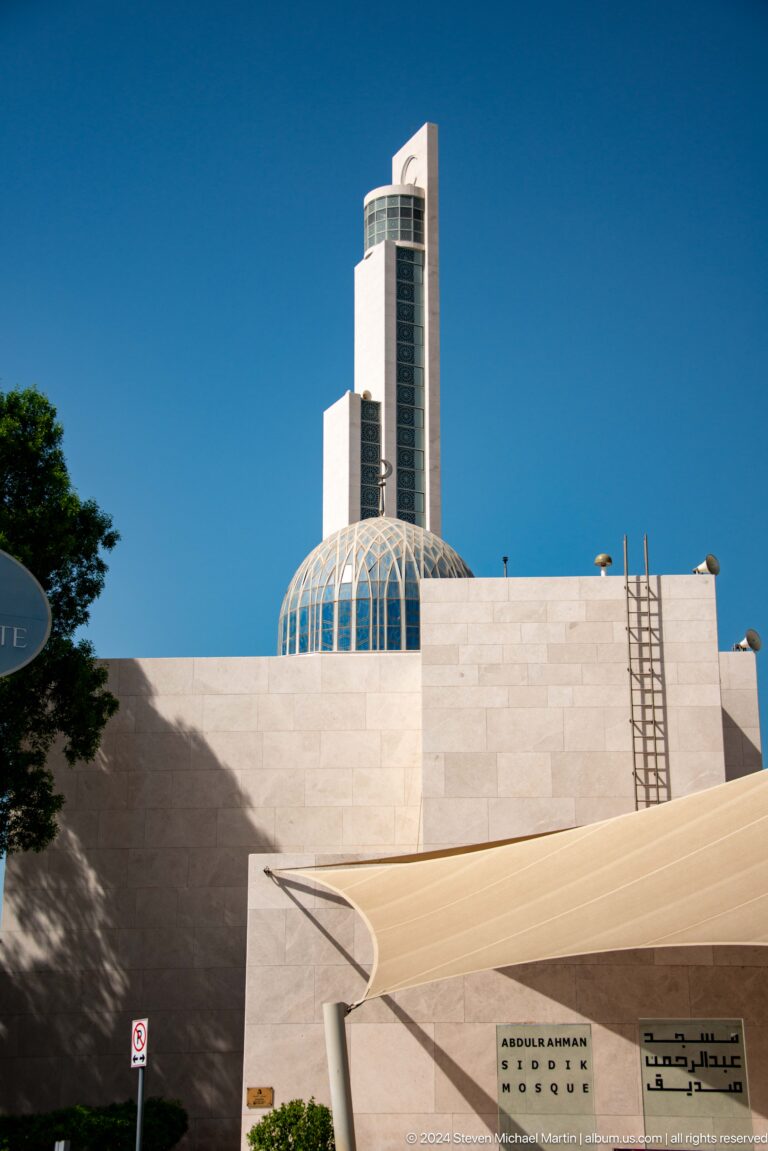 White modern mosque with a ribbed glass dome and tall rectangular minaret.
