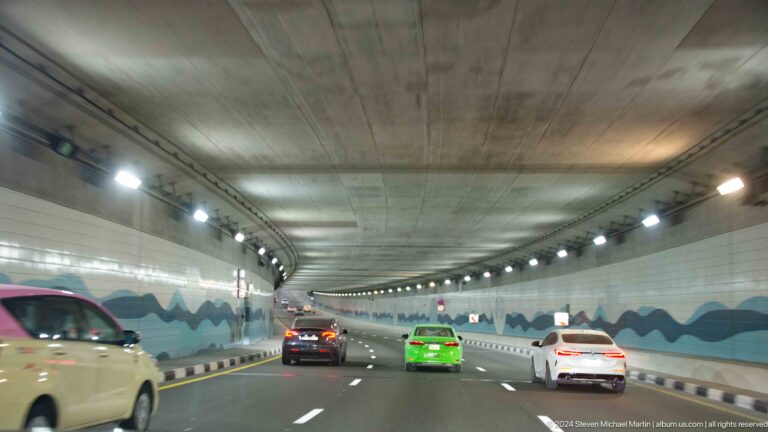 Cars traveling through a broad concrete tunnel with blue wave graphics.
