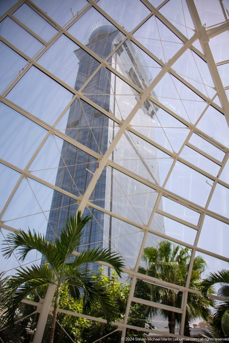 White steel-and-glass atrium roof framing a blue-glass tower and palm fronds.