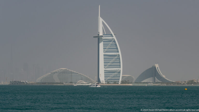 Burj Al Arab and curving Jumeirah resort buildings seen across open sea.
