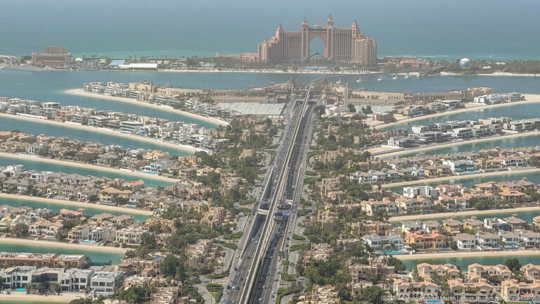 Long aerial view along Palm Jumeirah's trunk and fronds toward Atlantis The Palm.