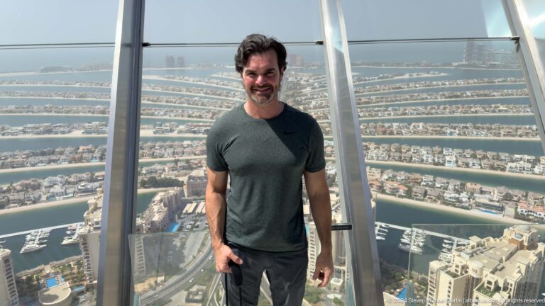 Man in a dark green shirt posing on an observation deck above Palm Jumeirah.