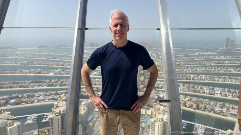 White-haired man in a navy shirt posing above Palm Jumeirah's fronds.