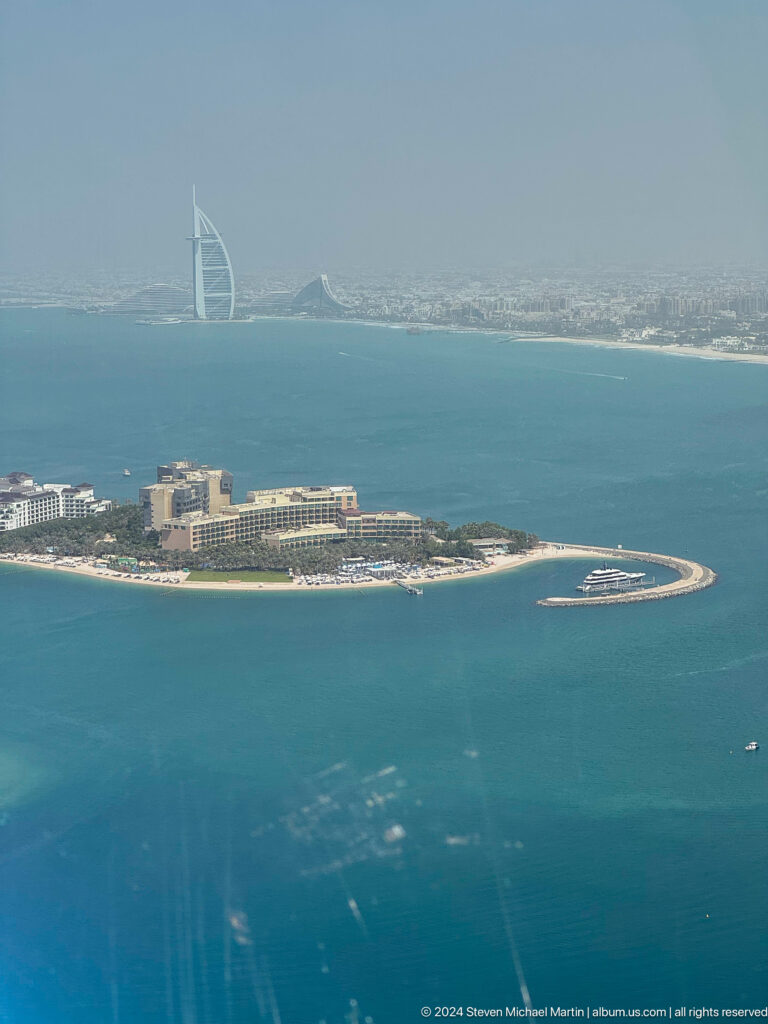 High view of a small Palm Jumeirah resort with beach, yacht, and curved breakwater.
