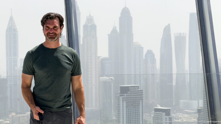 Man in a dark green shirt posing before the hazy Dubai Marina skyline.