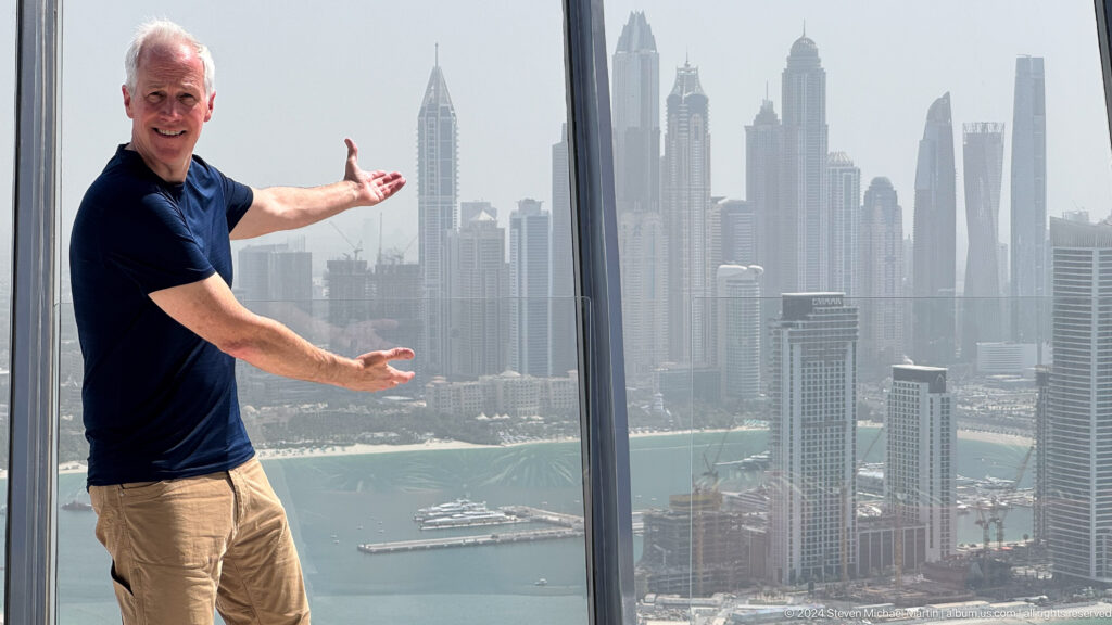 White-haired man extending his arms toward the Dubai Marina skyline.