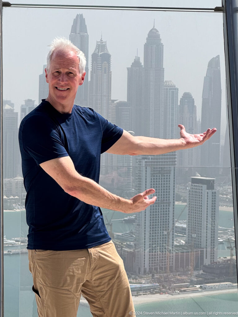 Close crop of a man extending his arms in front of Dubai Marina towers.