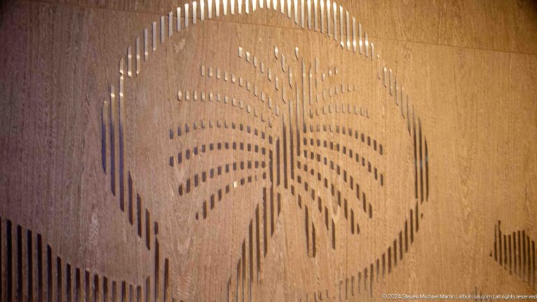 Backlit wooden wall panel perforated in the shape of a palm tree.
