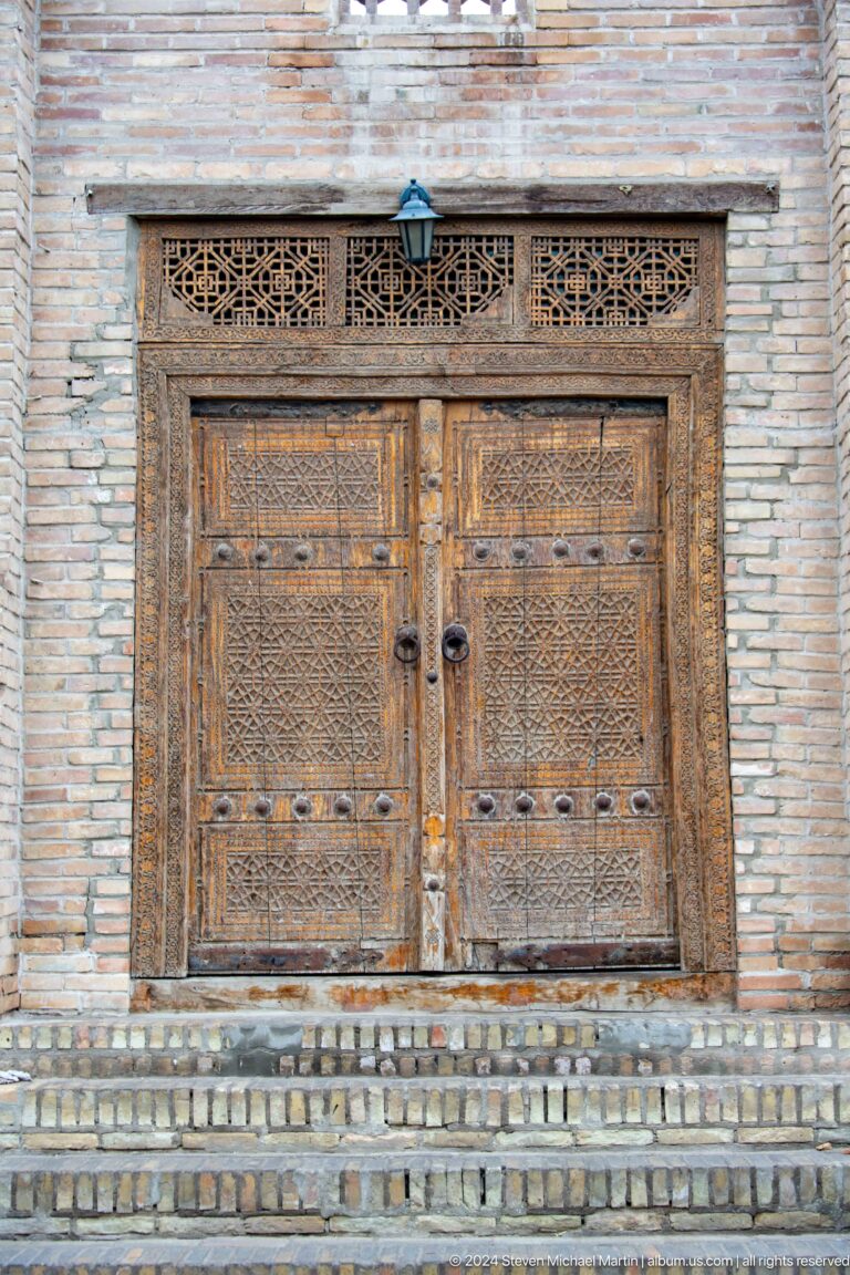 Carved wooden double doors in brick wall.